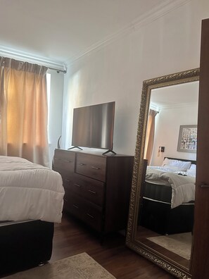 Une chambre à coucher comprenant un lit, une commode, un téléviseur et un grand miroir.