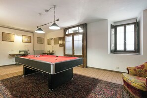 Taula de bitlles en una habitació amb un mosaic de catifes, una cadira i una finestra amb cortines.