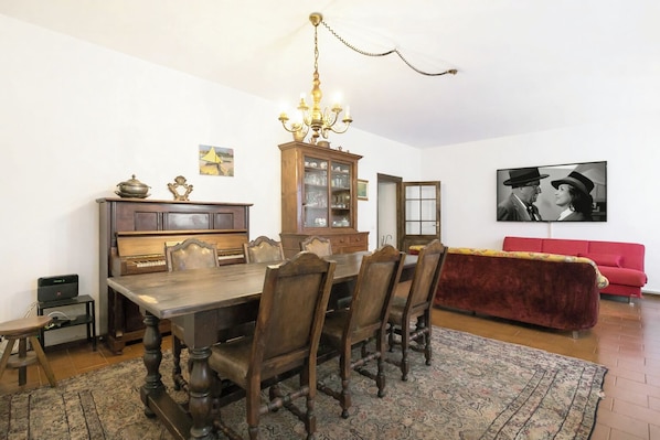 A dining area with a wooden table and chairs, a chandelier, a cabinet with glassware, and a red sofa.