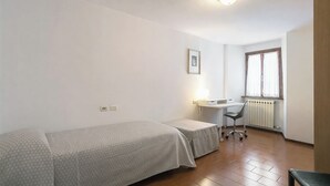 A small, clean room with a single bed, a desk, and a chair.