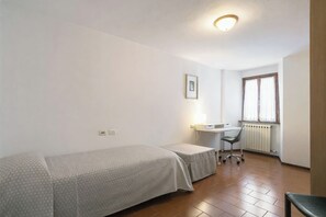 A small, clean room with a single bed, a desk, and a chair.