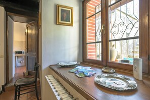 A kitchen with a wooden countertop, a microwave, a window with decorative iron bars, and a framed picture on the wall.
