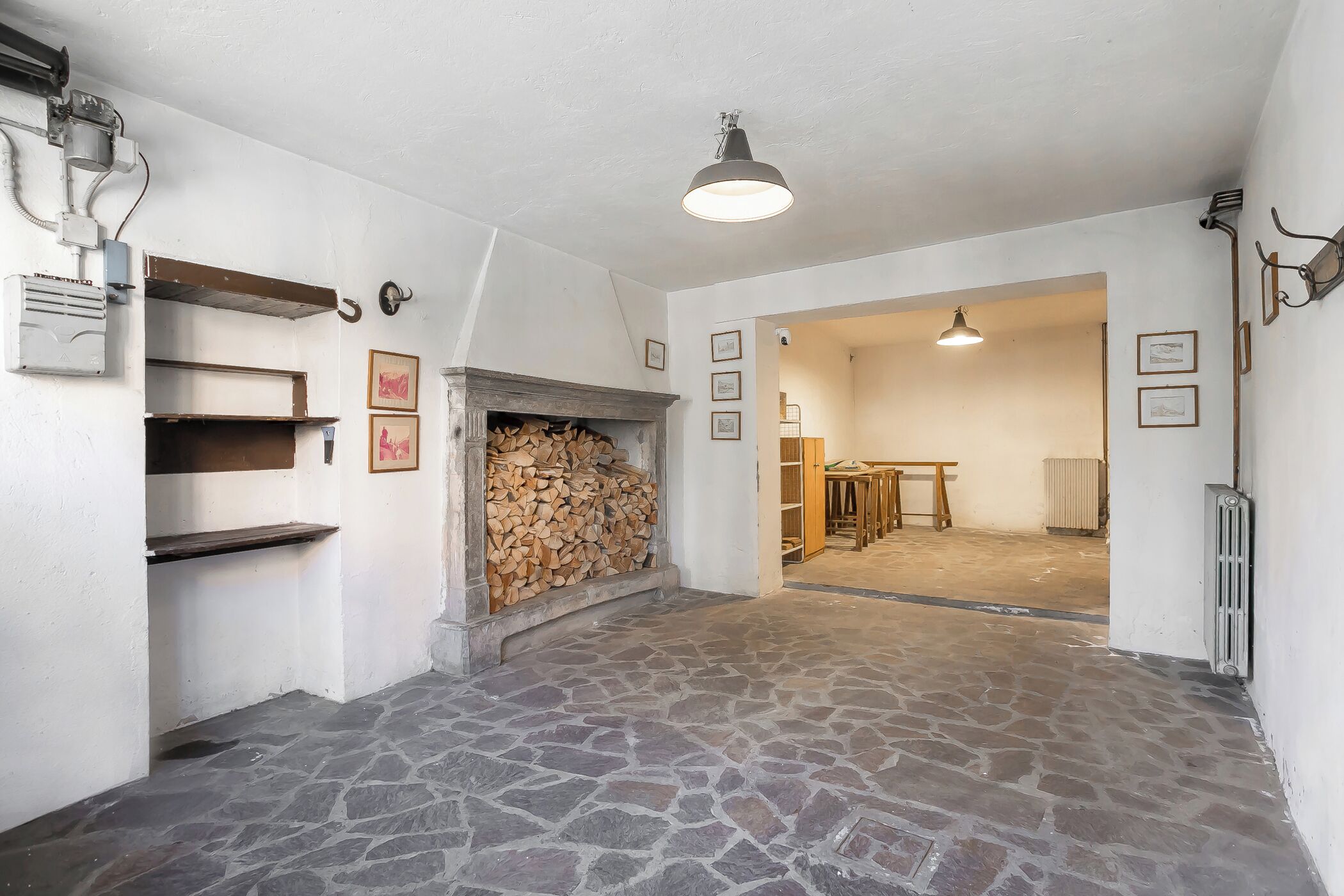 A room with a stone floor, a fireplace with wood, and a door leading to another room.