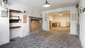 A room with a stone floor, a fireplace with wood, and a door leading to another room.