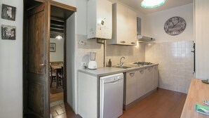 A compact kitchen with a dishwasher, a stove, and a sink. There is a clock on the wall and a door leading to another room.