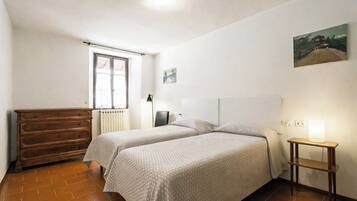 A bedroom with two beds, a dresser, a radiator, a window, and a painting on the wall.