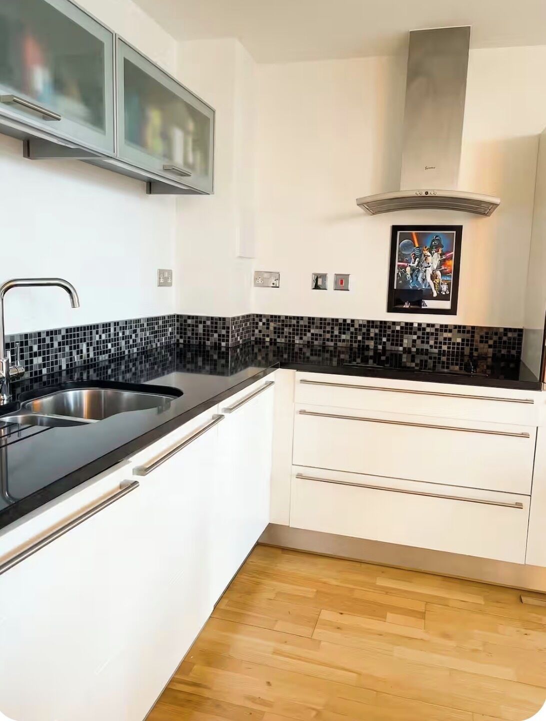 A modern kitchen with a black and white tiled backsplash, stainless steel sink, and white cabinetry.
