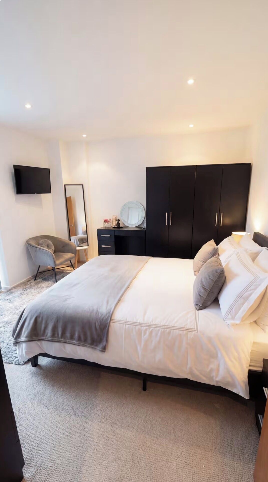 Ein modernes Schlafzimmer mit einem großen Bett, einem Schreibtisch, einem Stuhl, einem Kleiderschrank und einem flachbildfernseher an der Wand.