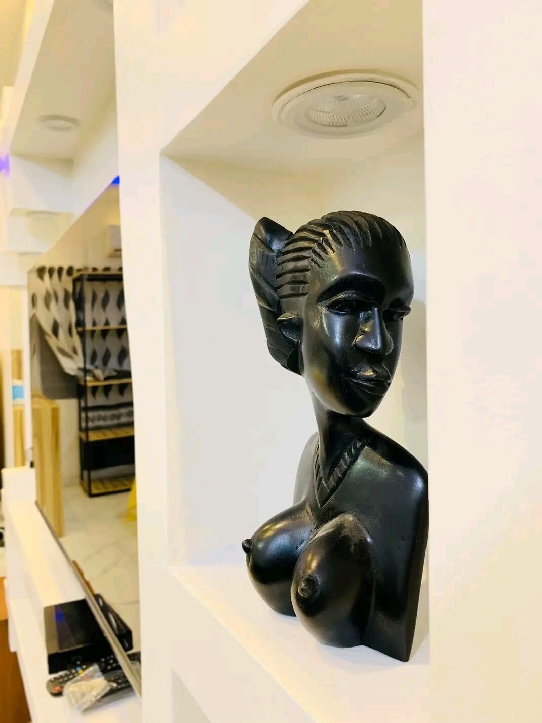 Eine Skulptur einer menschlichen Figur steht auf einem weißen Regal in einem Zimmer mit weißen Wänden und einem gefliesten Boden.