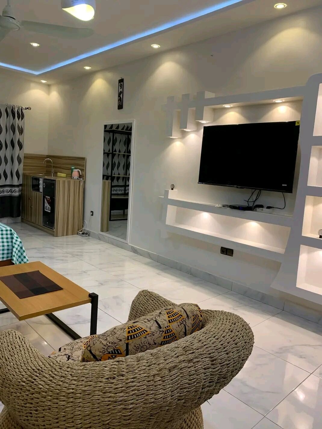 Una sala moderna con un televisor de pantalla plana montado en una pared blanca, un sofá tejido y una pequeña mesa de madera.