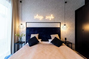 A modern bedroom with a dark headboard, a neon sign that reads 'stay safe,' and two bedside lamps. - Sienna 8D | Comfortable Apartment | Parking (Stronie Śląskie)