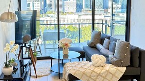 A modern living room with a sofa, a coffee table, and a TV. There is a balcony with a city view. - Prime 2BR Location - Pool & Parking @BCT 1004 (South Brisbane)