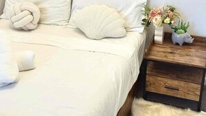 A bed with a white comforter and pillows, a wooden nightstand with a vase of flowers, and a fluffy white rug. - Prime 2BR Location - Pool & Parking @BCT 1004 (South Brisbane)