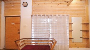 Una habitación de madera con un banco, una puerta, una ventana con cortinas y un reloj de pared.
