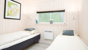 A room with two beds, a window with a view of trees, a radiator, and a framed picture on the wall. - Grobenbrode Baltic Horizon Haven (Grossenbrode)