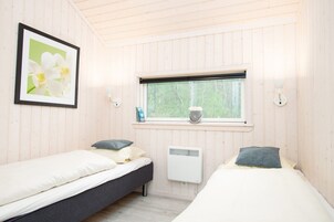 A room with two beds, a window with a view of trees, a radiator, and a framed picture on the wall.