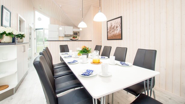 A modern dining area with a long table, black chairs, white plates, and a white ceiling. - Grobenbrode Baltic Horizon Haven (Grossenbrode)