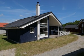 Ein kleines, eingeschossiges Gebäude mit einem geneigten Dach, einem Schornstein und einer überdachten Veranda.