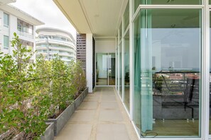 A modern residential building with a glass door entrance, a balcony with plants, and a view of other buildings. - Exquisite Sea View Luxury Apartment by the Veloche Group (Tambon Karon)
