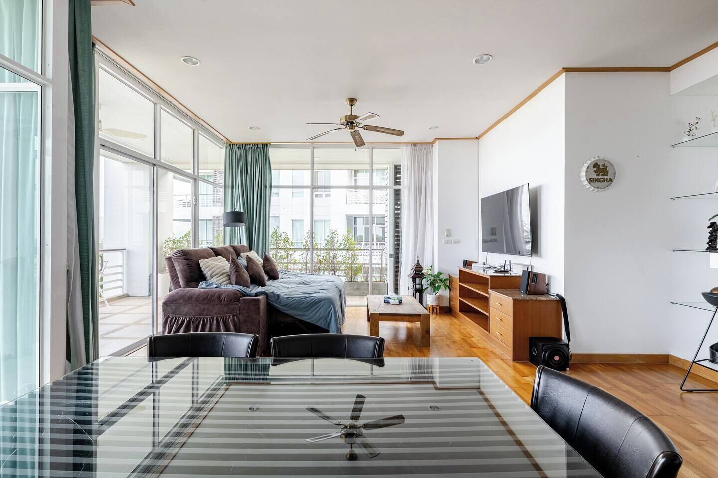 Een moderne woonkamer met een glazen eettafel, een bank, een televisie en een plafondventilator.
