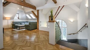 Un loft spacieux doté d’un parquet en chevrons, d’un escalier avec une rampe en verre et d’un coin salon confortable avec un canapé et une table basse.