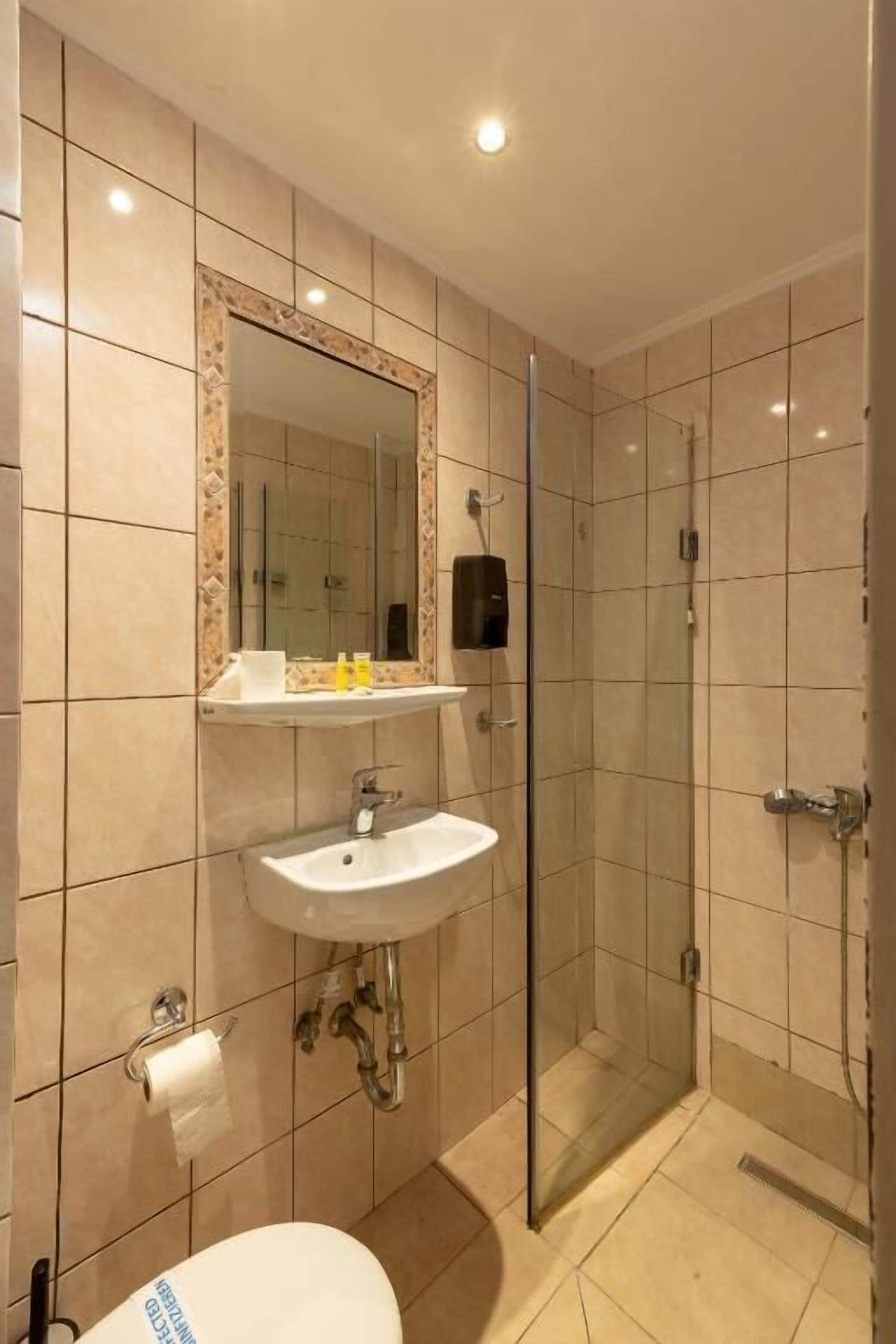 A bathroom with a toilet, sink, mirror, and shower.