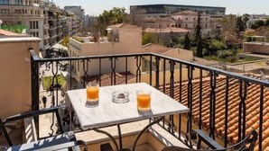 A balcony with a table and chairs, overlooking a cityscape with buildings and a clear sky.