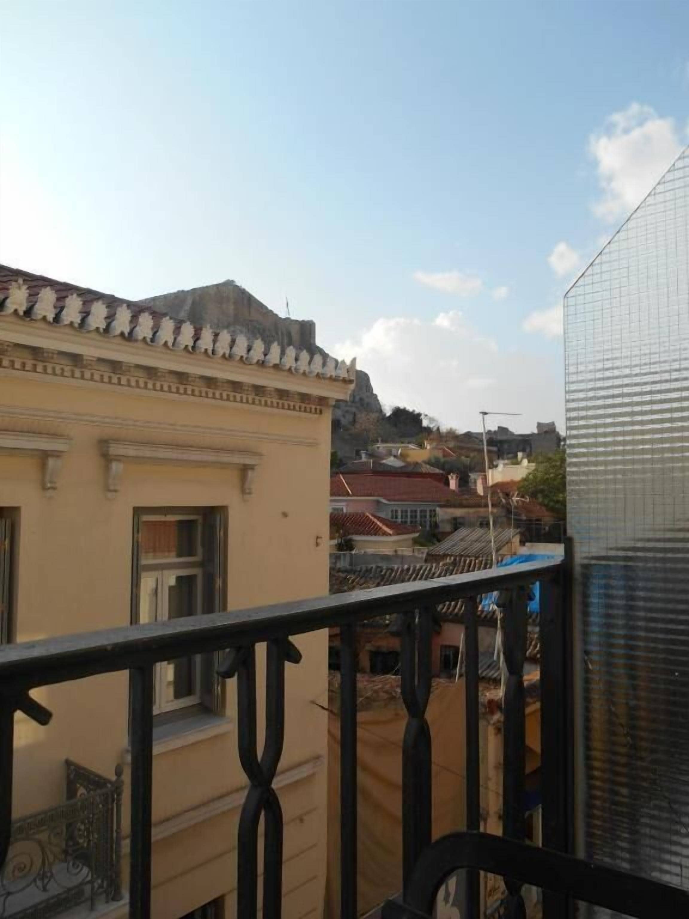 Un balcón con barandilla de metal que da a un paisaje urbano con edificios y cielo despejado.
