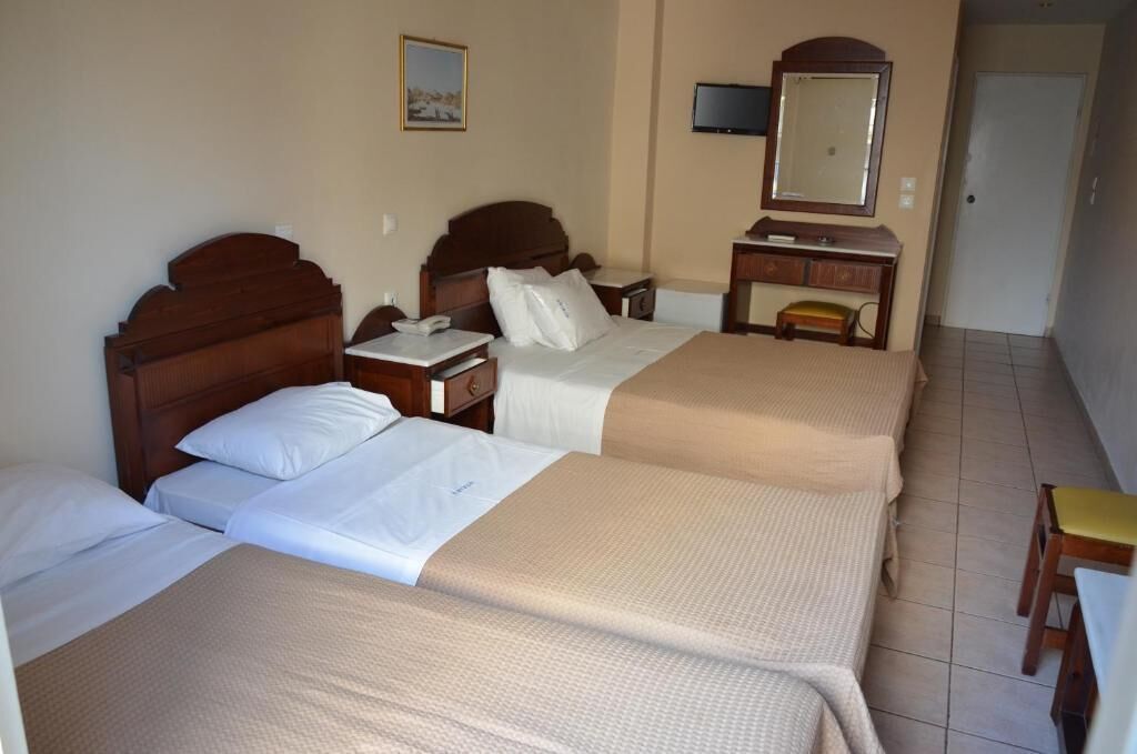 A hotel room with three beds, a bedside table with a lamp, a TV, and a mirror.