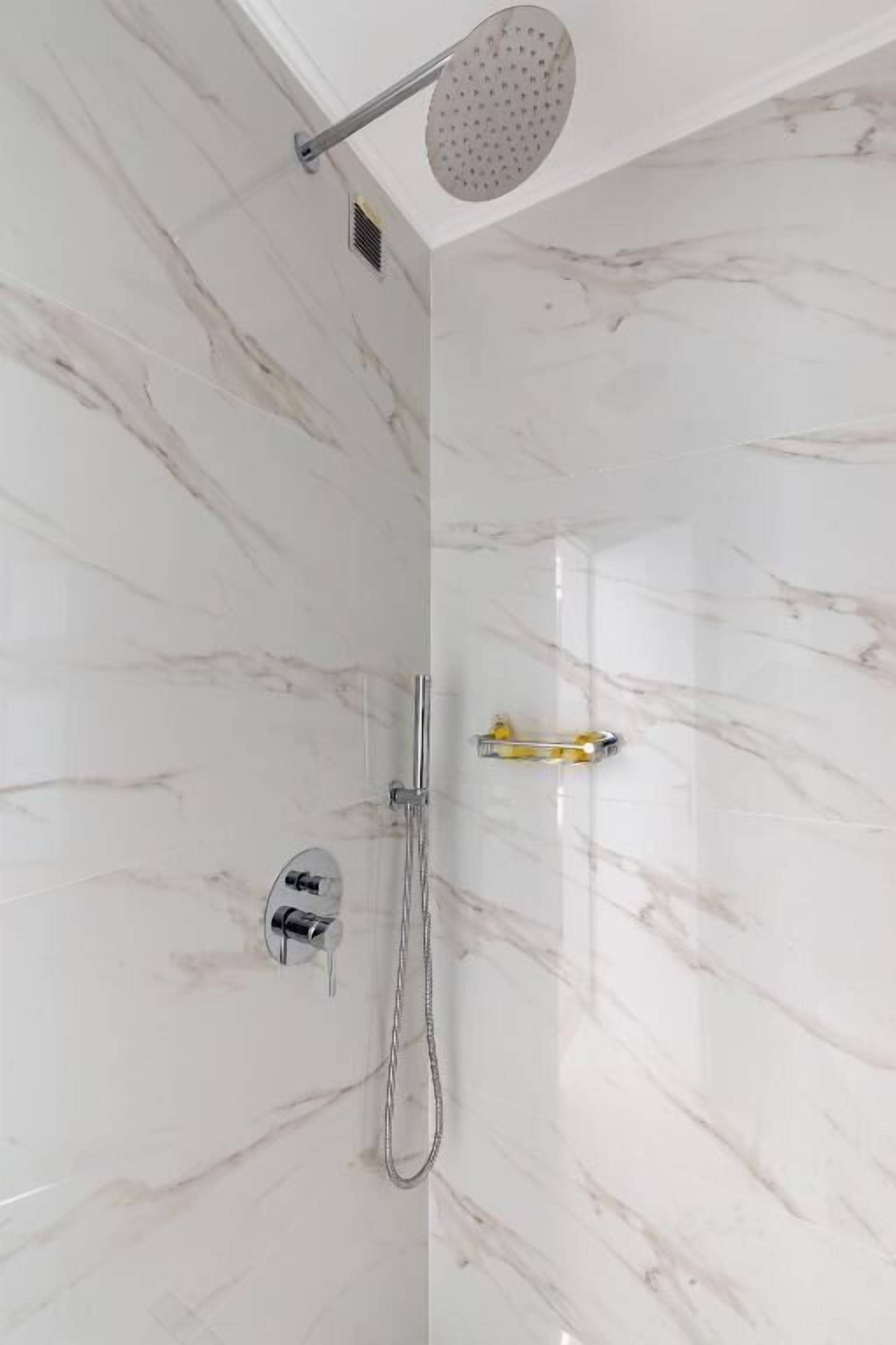 A shower with a handheld showerhead and a wall-mounted control panel.