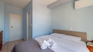 A hotel room with a bed, a bedside table, a chair, a door, and an air conditioning unit.