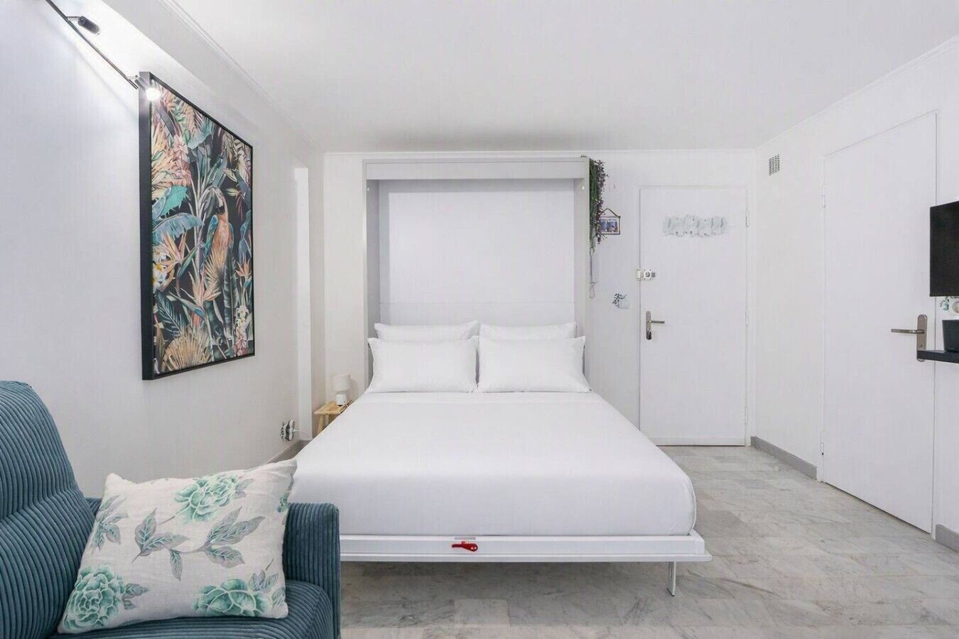 Ein Hotelzimmer mit einem Bett, einem Sessel, einem Bild an der Wand und einer Tür.
