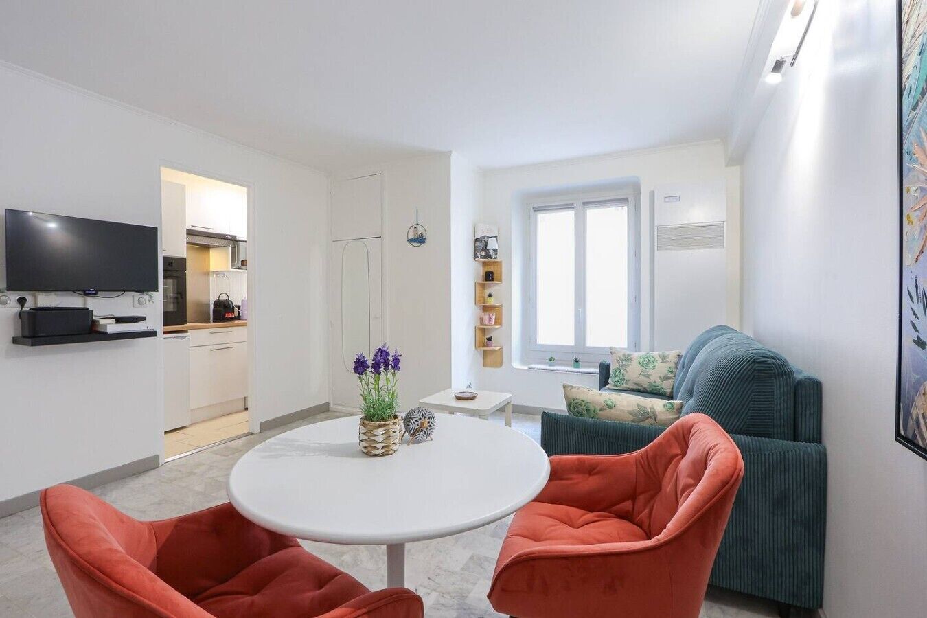 A modern living room with a round table, two orange chairs, a green sofa, and a television mounted on the wall.