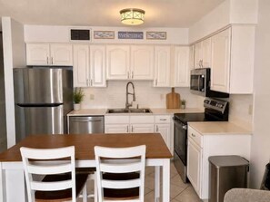 A kitchen with white cabinets, stainless steel appliances, a wooden dining table, and two chairs. - Saltystaysal (Orange Beach)