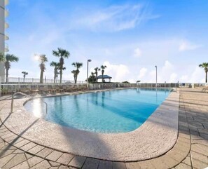 A swimming pool with a curved edge, surrounded by a tiled deck and palm trees. - Saltystaysal (Orange Beach)