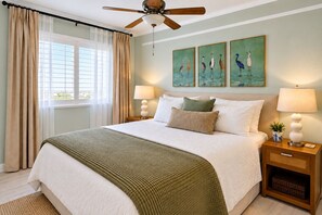 A bedroom with a bed, two bedside tables, a ceiling fan, a window with curtains, and wall art. - Saltystaysal-Oceanfront views in Orange Beach, Alabama! (Orange Beach)