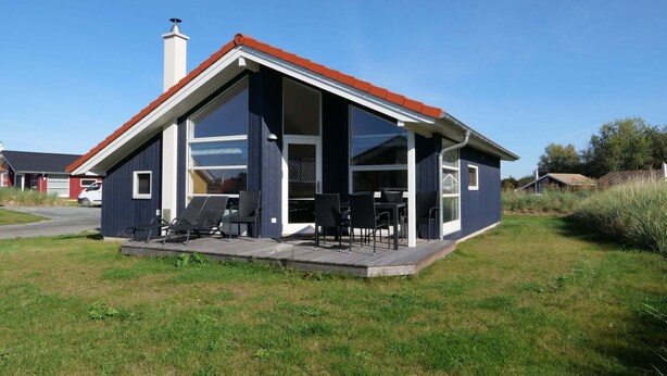 A modern house with a large glass front, a covered patio with outdoor furniture, and a red roof. - Charmante Sauna-hutte fur 6 Personen (Grossenbrode)