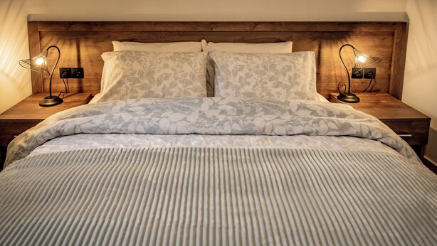 A neatly made bed with a floral-patterned duvet, flanked by two bedside tables with lamps, in a room with wooden headboard and nightstands.