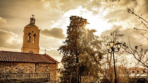 A stone building with a clock tower, surrounded by trees and a paved area.
