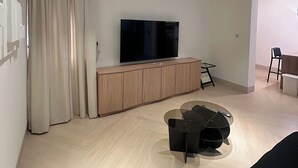 Una sala de estar moderna con televisor de pantalla plana, mueble de madera y un comedor con mesa y sillas.