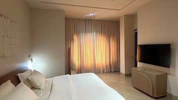 A modern hotel room with a large bed, a flat-screen TV, and a large window with curtains.