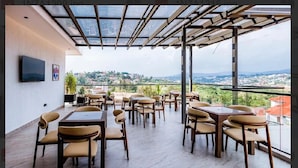 Una terraza en la azotea con mesas y sillas, un televisor de pantalla plana y vistas a la ciudad.