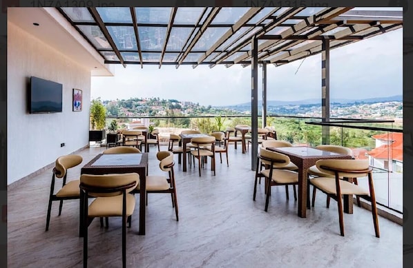 A rooftop terrace with tables and chairs, a flat-screen TV, and a city view.