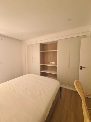 A bedroom with a bed, a wardrobe with multiple compartments, and a chair. - Palace Vista · Luxury 2-Bedroom Apartment Across from Savoy Palace (Funchal)