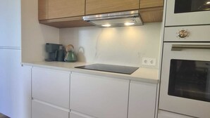 Moderni keittiö, jossa on valkoiset kaapit, puinen yläosa, sisäänrakennettu uuni ja vedenkeitin työtasolla.