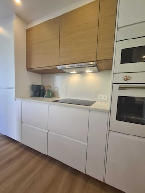 Eine moderne Küche mit weißen Schränken, einem Holdbereich oben, einem eingebauten Backofen und einem Wasserkocher auf der Arbeitsplatte.