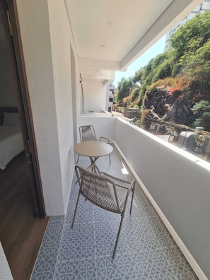 A balcony with a table and chairs, a patterned floor, and a view of greenery and buildings. - Palace Vista · Luxury 2-Bedroom Apartment Across from Savoy Palace (Funchal)