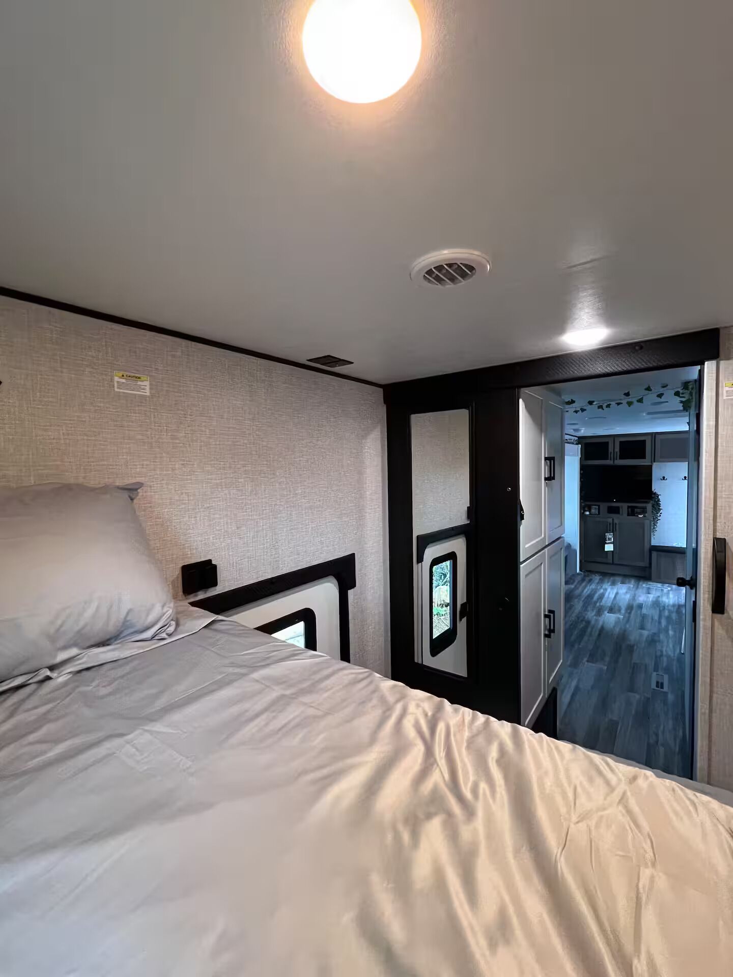 Un dormitorio con cama, cabecera, lámpara de pared y puerta que da al baño.