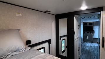 Quarto com cama, cabeceira, luminária na parede e porta para um banheiro.