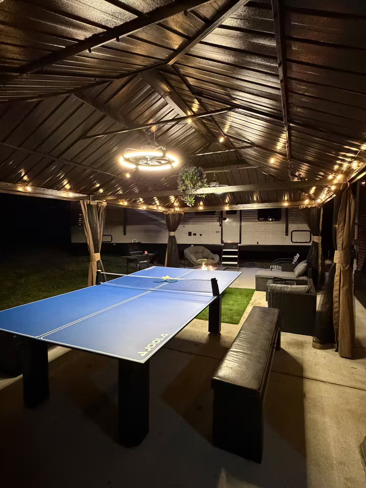 Un espacio recreativo al aire libre con mesa de ping pong, bancos y una zona de estar techada.